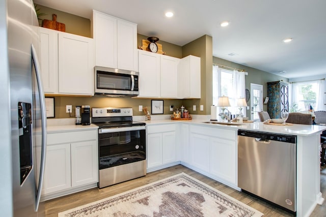 kitchen featuring sink, stainless steel appliances, kitchen peninsula, light hardwood / wood-style floors, and white cabinets