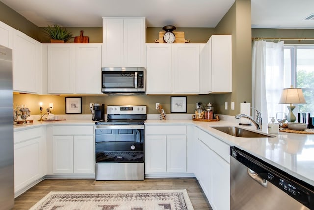 kitchen with light wood-type flooring, stainless steel appliances, white cabinetry, and sink