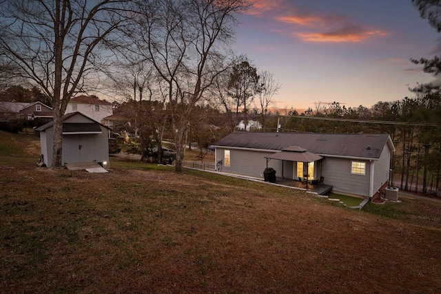 back house at dusk with a yard, central AC unit, a shed, a gazebo, and a patio