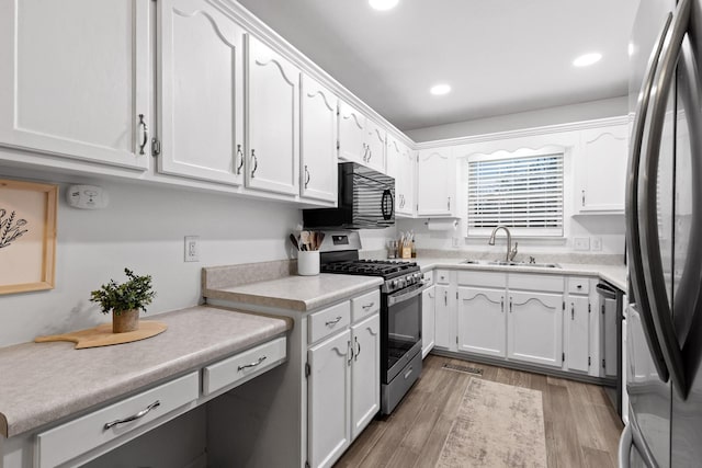 kitchen with sink, white cabinets, light hardwood / wood-style floors, and appliances with stainless steel finishes