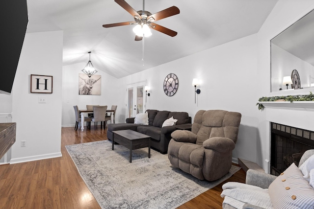 living room featuring lofted ceiling, wood-type flooring, and ceiling fan with notable chandelier