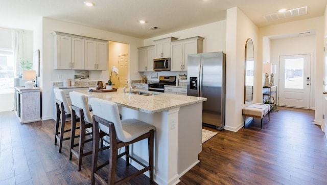 kitchen featuring a breakfast bar, stainless steel appliances, light stone countertops, and a center island with sink