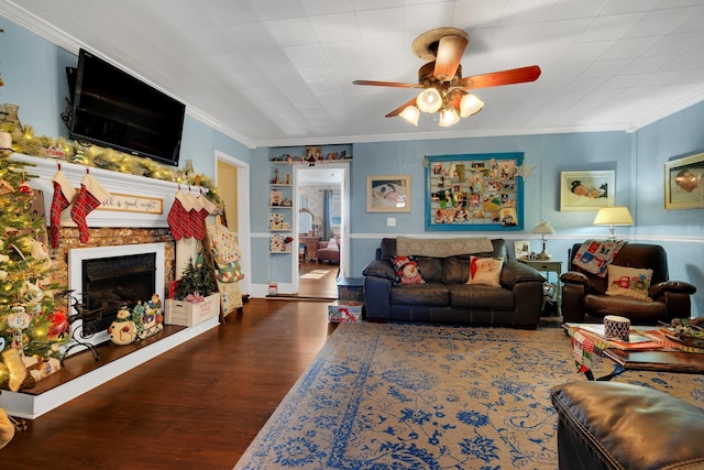 living room featuring a stone fireplace, hardwood / wood-style flooring, ceiling fan, and ornamental molding