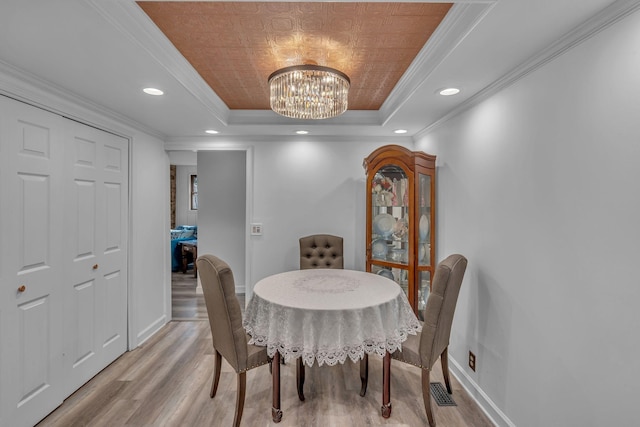 dining space with a tray ceiling, an inviting chandelier, ornamental molding, and light hardwood / wood-style flooring