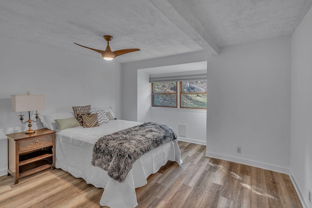 bedroom featuring beam ceiling, ceiling fan, hardwood / wood-style floors, and a textured ceiling