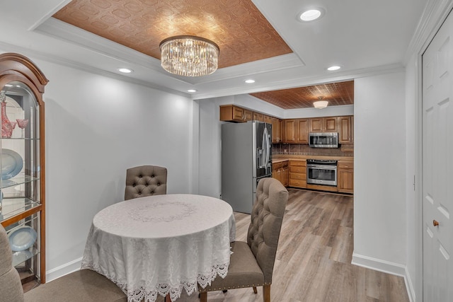 dining room featuring light wood-style flooring, a raised ceiling, baseboards, and ornamental molding