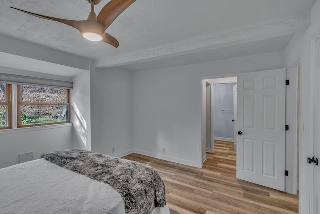 bedroom with beamed ceiling, ceiling fan, a textured ceiling, and light hardwood / wood-style flooring