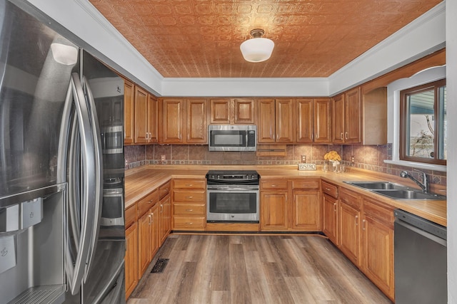 kitchen featuring crown molding, sink, tasteful backsplash, light hardwood / wood-style floors, and stainless steel appliances