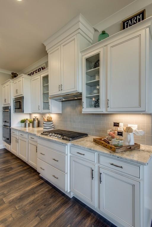 kitchen featuring light stone countertops, dark wood-type flooring, stainless steel appliances, backsplash, and white cabinets