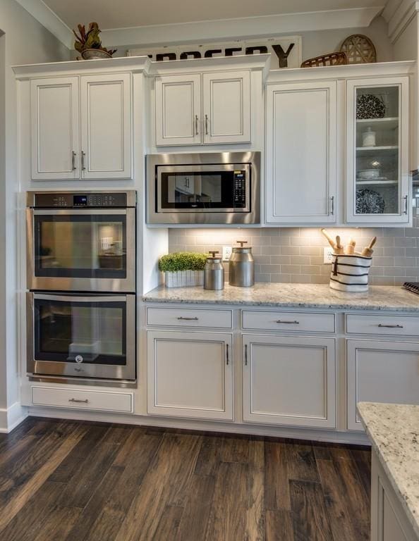 kitchen with dark wood-type flooring, stainless steel appliances, tasteful backsplash, light stone counters, and white cabinets