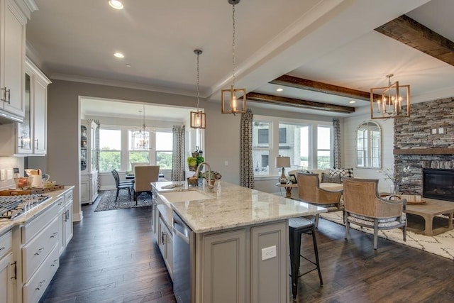 kitchen featuring white cabinetry, a stone fireplace, a kitchen island with sink, and decorative light fixtures