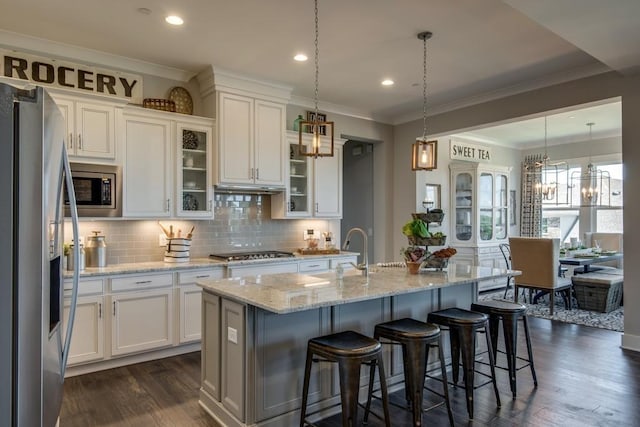 kitchen featuring hanging light fixtures, stainless steel appliances, a kitchen breakfast bar, an island with sink, and white cabinets