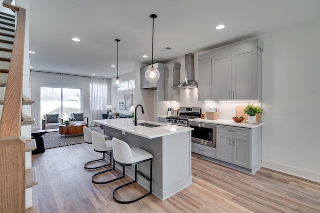 kitchen featuring pendant lighting, appliances with stainless steel finishes, wall chimney exhaust hood, sink, and gray cabinetry