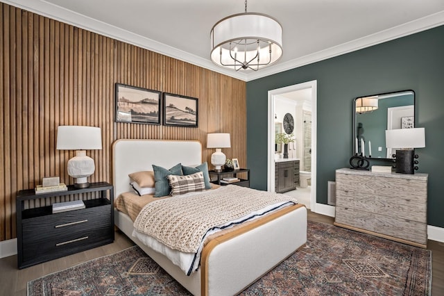 bedroom with wooden walls, dark wood-type flooring, crown molding, a chandelier, and connected bathroom