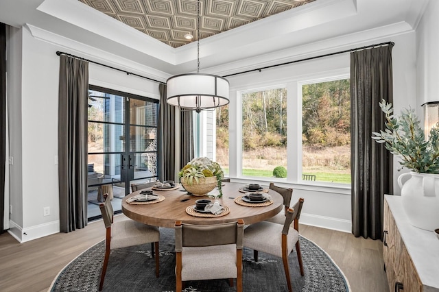 dining space with light hardwood / wood-style floors, a raised ceiling, and crown molding