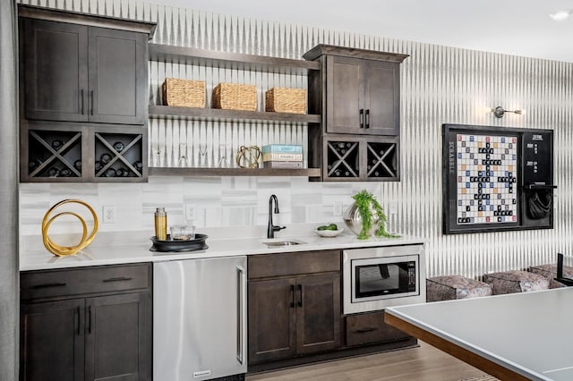 bar featuring light wood-type flooring, fridge, dark brown cabinetry, sink, and stainless steel microwave