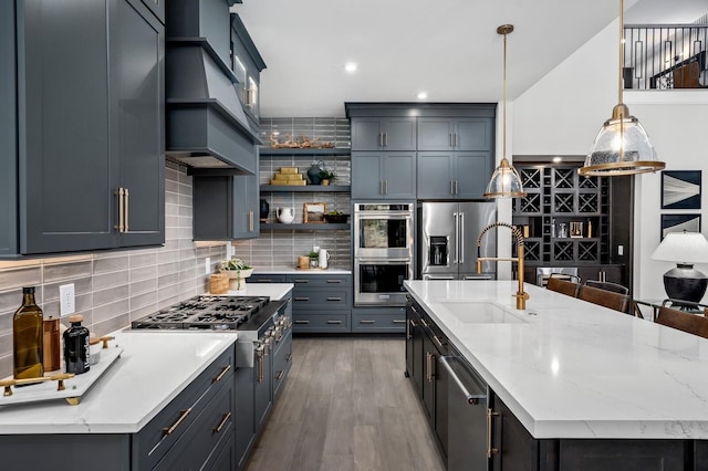 kitchen featuring stainless steel appliances, backsplash, hardwood / wood-style floors, an island with sink, and decorative light fixtures