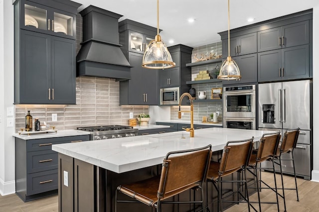 kitchen with premium range hood, an island with sink, hanging light fixtures, and appliances with stainless steel finishes