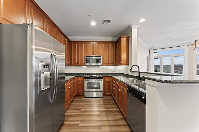 kitchen featuring sink, kitchen peninsula, crown molding, dark stone counters, and appliances with stainless steel finishes