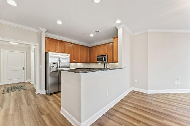 kitchen featuring dark stone counters, crown molding, light wood-type flooring, kitchen peninsula, and stainless steel appliances