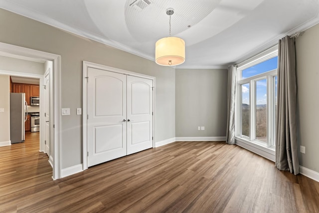 unfurnished bedroom featuring stainless steel fridge, wood-type flooring, ornamental molding, and a closet