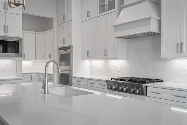 kitchen featuring white cabinets, light stone countertops, premium range hood, and appliances with stainless steel finishes