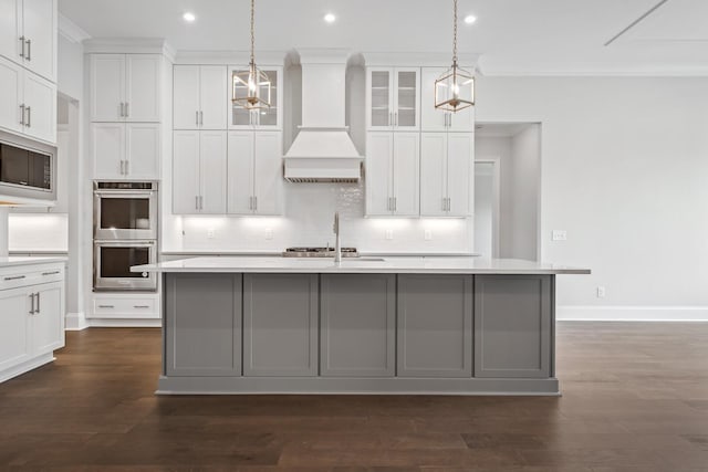 kitchen featuring stainless steel appliances, decorative light fixtures, a center island with sink, white cabinets, and custom exhaust hood