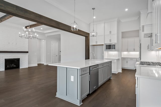 kitchen with a kitchen island with sink, sink, a brick fireplace, white cabinetry, and stainless steel appliances