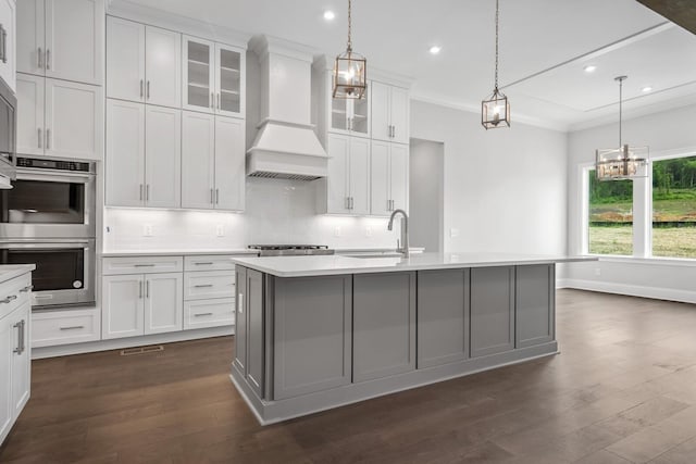 kitchen with premium range hood, a center island with sink, white cabinets, sink, and stainless steel double oven