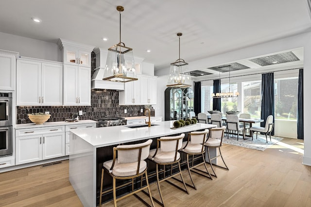 kitchen with custom exhaust hood, a kitchen island with sink, sink, white cabinets, and range