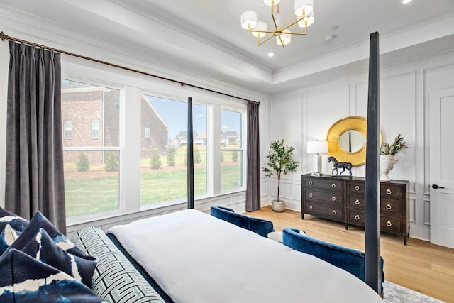 bedroom featuring a raised ceiling, hardwood / wood-style floors, a chandelier, and ornamental molding