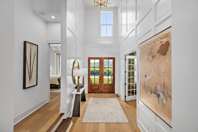 foyer entrance with french doors, a towering ceiling, a chandelier, and light wood-type flooring