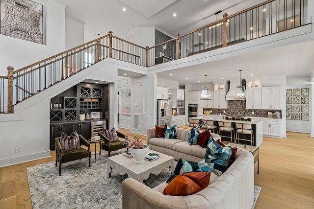 living room with beverage cooler, light hardwood / wood-style floors, and a high ceiling