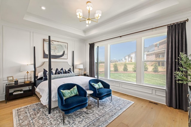 bedroom featuring a tray ceiling, crown molding, light hardwood / wood-style flooring, and a notable chandelier