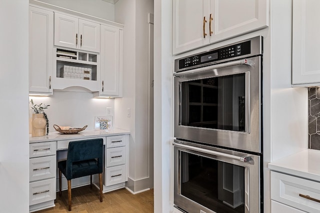 kitchen with white cabinets, stainless steel double oven, and light hardwood / wood-style flooring