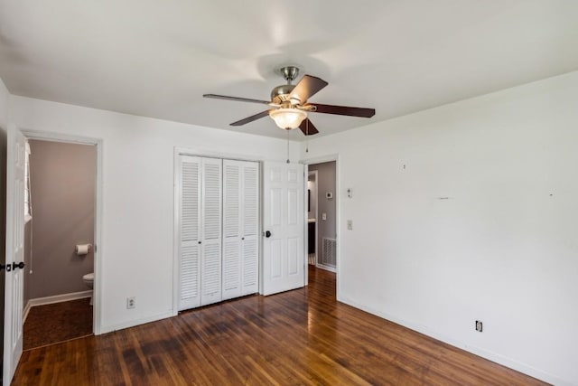 unfurnished bedroom featuring ceiling fan, ensuite bath, dark wood-type flooring, and a closet