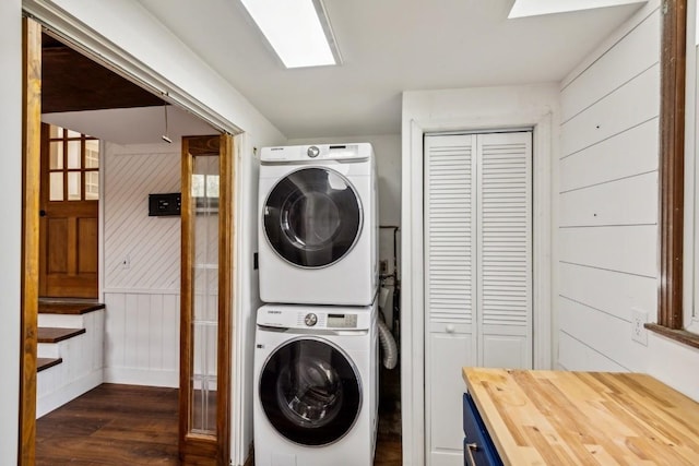 laundry area with dark hardwood / wood-style flooring, stacked washing maching and dryer, and wooden walls