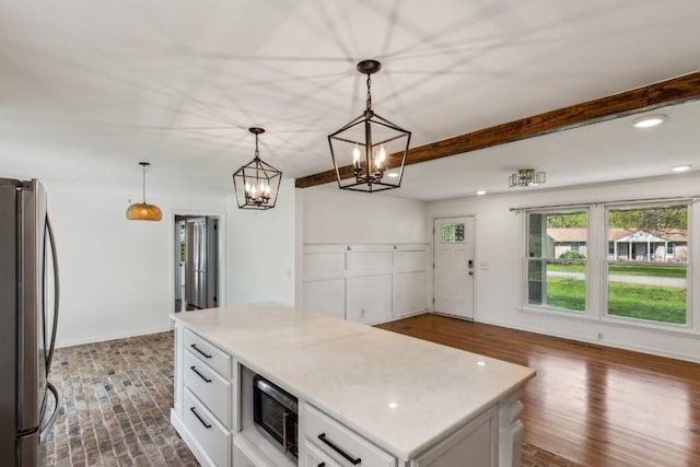 kitchen with stainless steel fridge, black microwave, decorative light fixtures, white cabinets, and a kitchen island