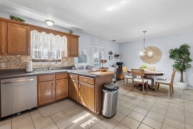 kitchen featuring decorative backsplash, brown cabinetry, a peninsula, stainless steel dishwasher, and a sink