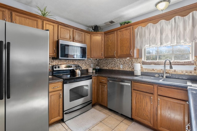 kitchen featuring stainless steel appliances, dark countertops, a sink, and brown cabinets