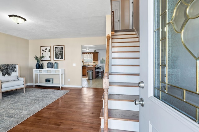 entryway with a fireplace with raised hearth, stairway, a textured ceiling, wood finished floors, and baseboards