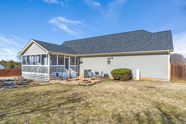 rear view of property with central air condition unit, a fire pit, fence, a sunroom, and a lawn