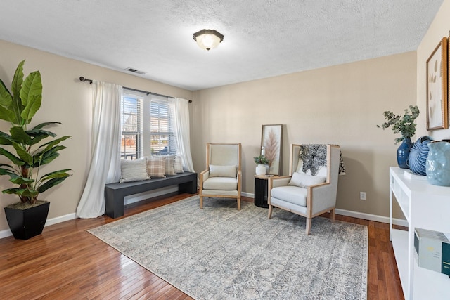 living area featuring hardwood / wood-style flooring, visible vents, baseboards, and a textured ceiling