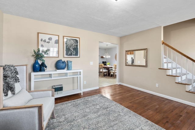 living room with a textured ceiling, wood finished floors, a chandelier, baseboards, and stairs