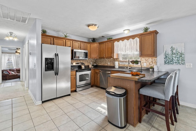 kitchen with tasteful backsplash, brown cabinetry, dark countertops, appliances with stainless steel finishes, and a peninsula