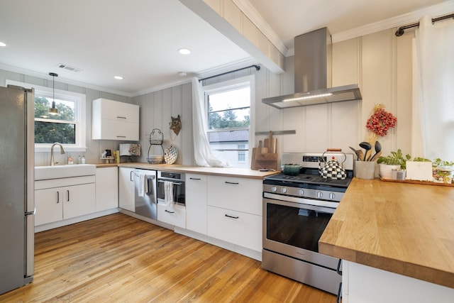 kitchen featuring white cabinetry, stainless steel appliances, wall chimney range hood, pendant lighting, and ornamental molding