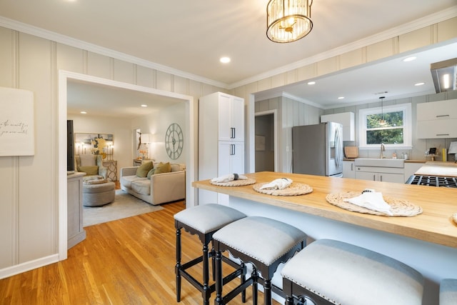 kitchen with a kitchen bar, stainless steel refrigerator with ice dispenser, crown molding, white cabinetry, and hanging light fixtures