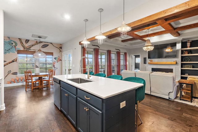 kitchen featuring sink, decorative light fixtures, dishwasher, a fireplace, and an island with sink