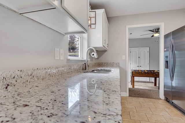 kitchen with stainless steel fridge, light stone counters, ceiling fan, sink, and white cabinetry