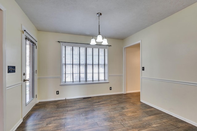 unfurnished dining area with a textured ceiling, dark hardwood / wood-style floors, and an inviting chandelier